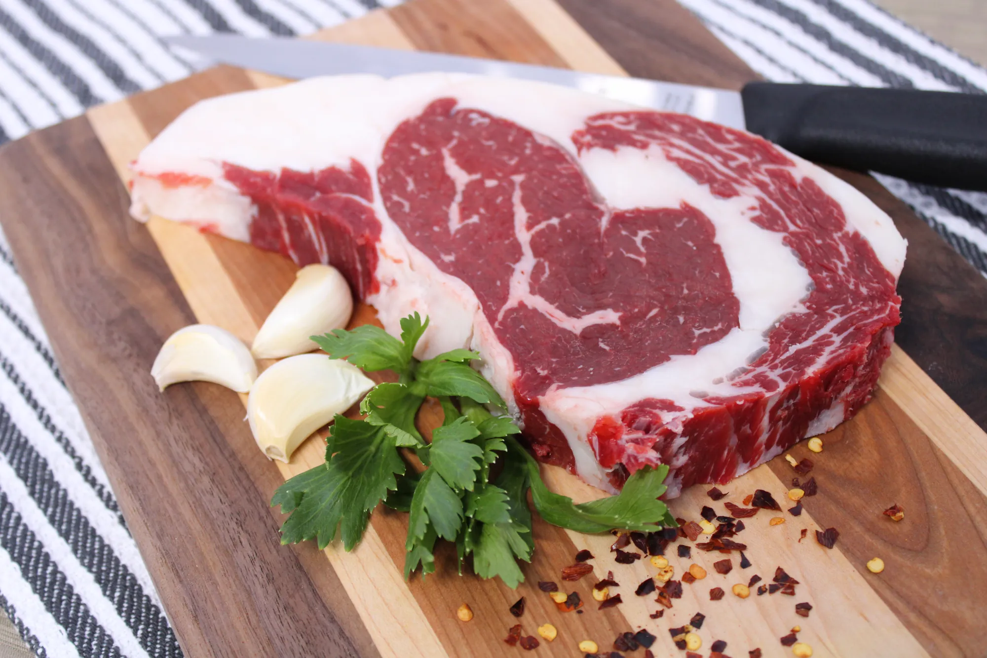 A thick-cut ribeye on a wooden board with garlic and parsley